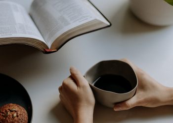 Muffin, hands around coffee mug and open bible